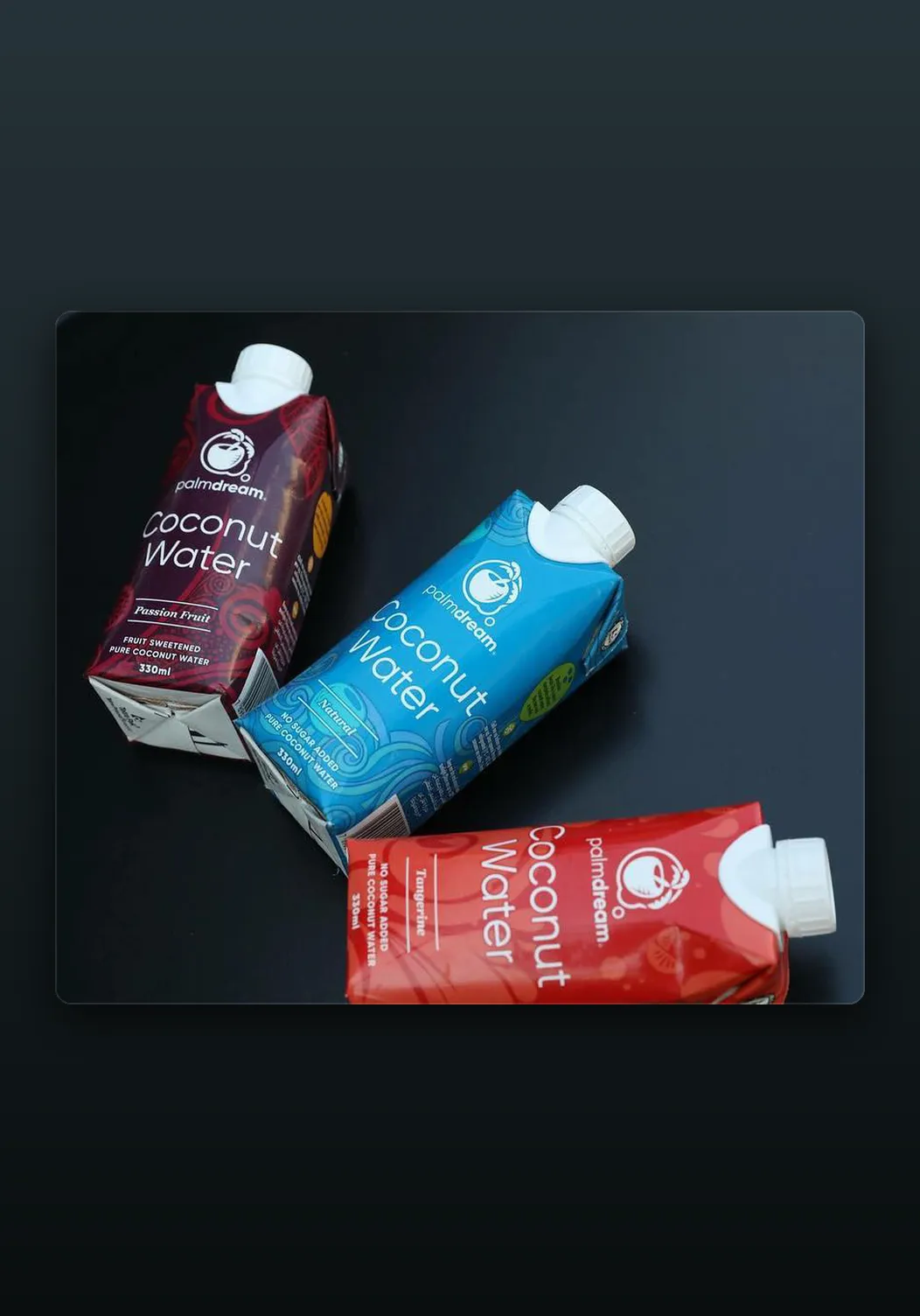Three Palmdream Coconut Water cartons in Passion Fruit, Natural, and Tangerine designs, photographed on a dark surface.